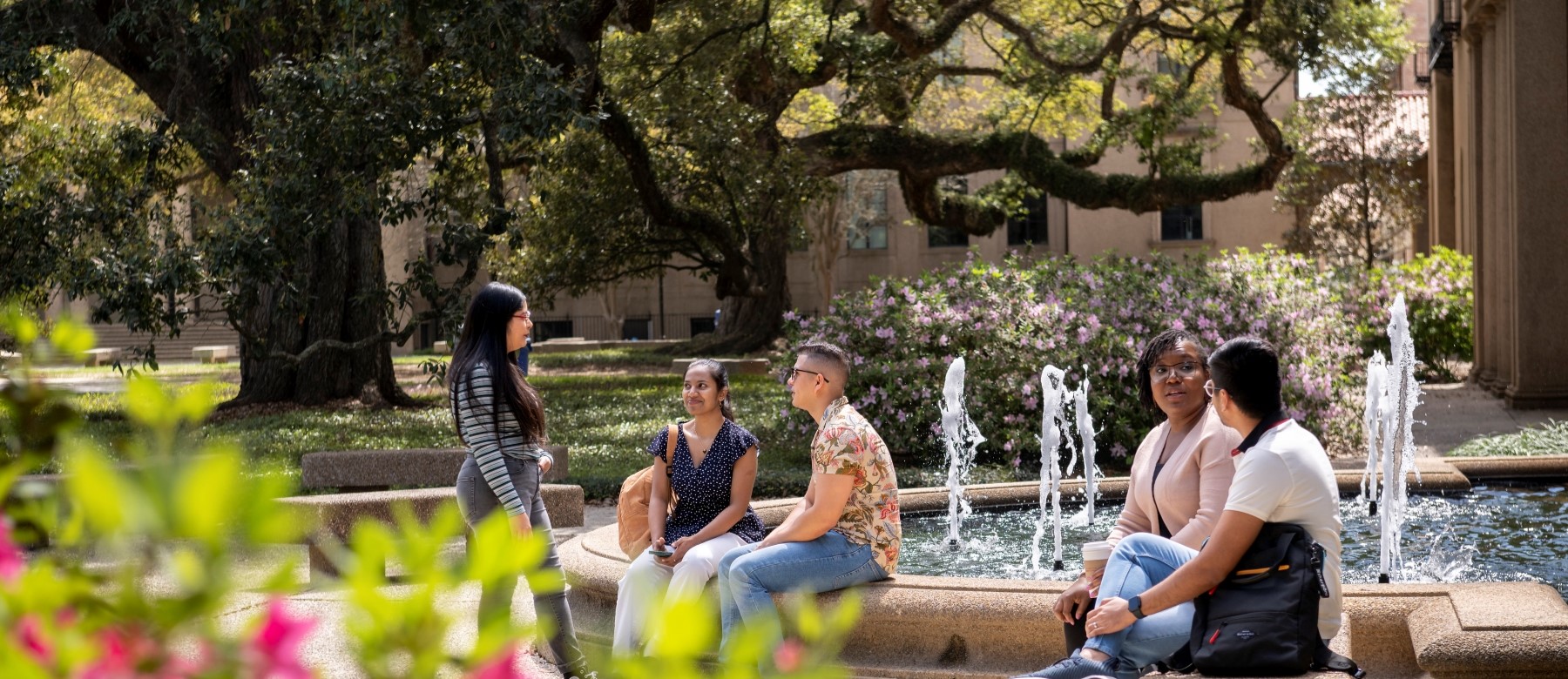 students sit outside on LSU's campus, near a fountain