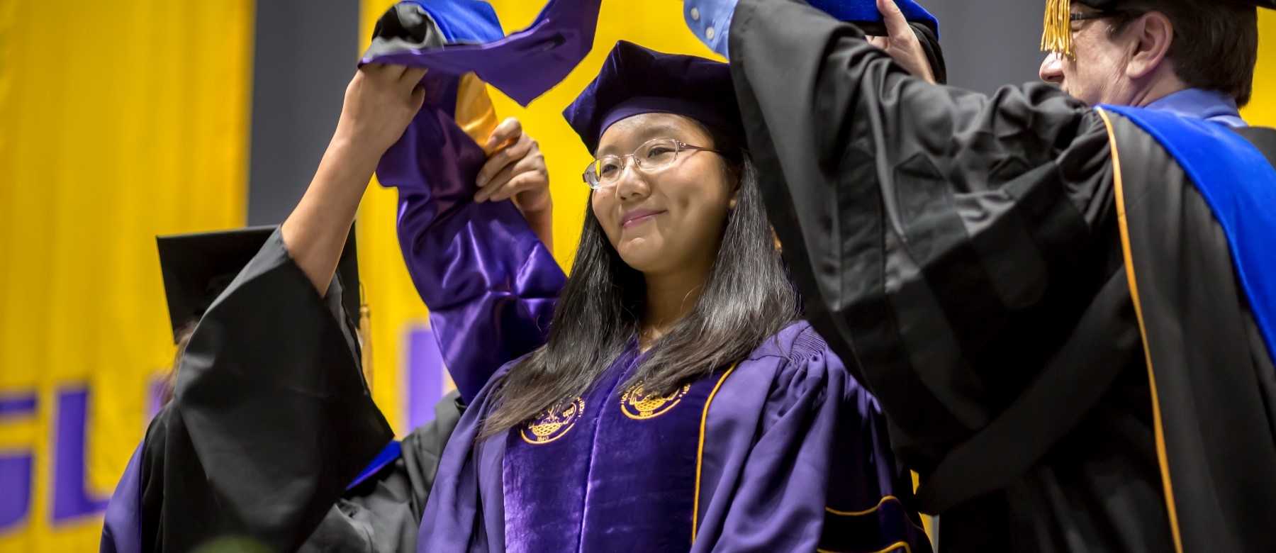 student smiles as two faculty members give her graduation regalia